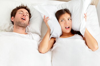 man snoring next to woman covering ears with pillows, sleep apnea and snoring Skokie, IL